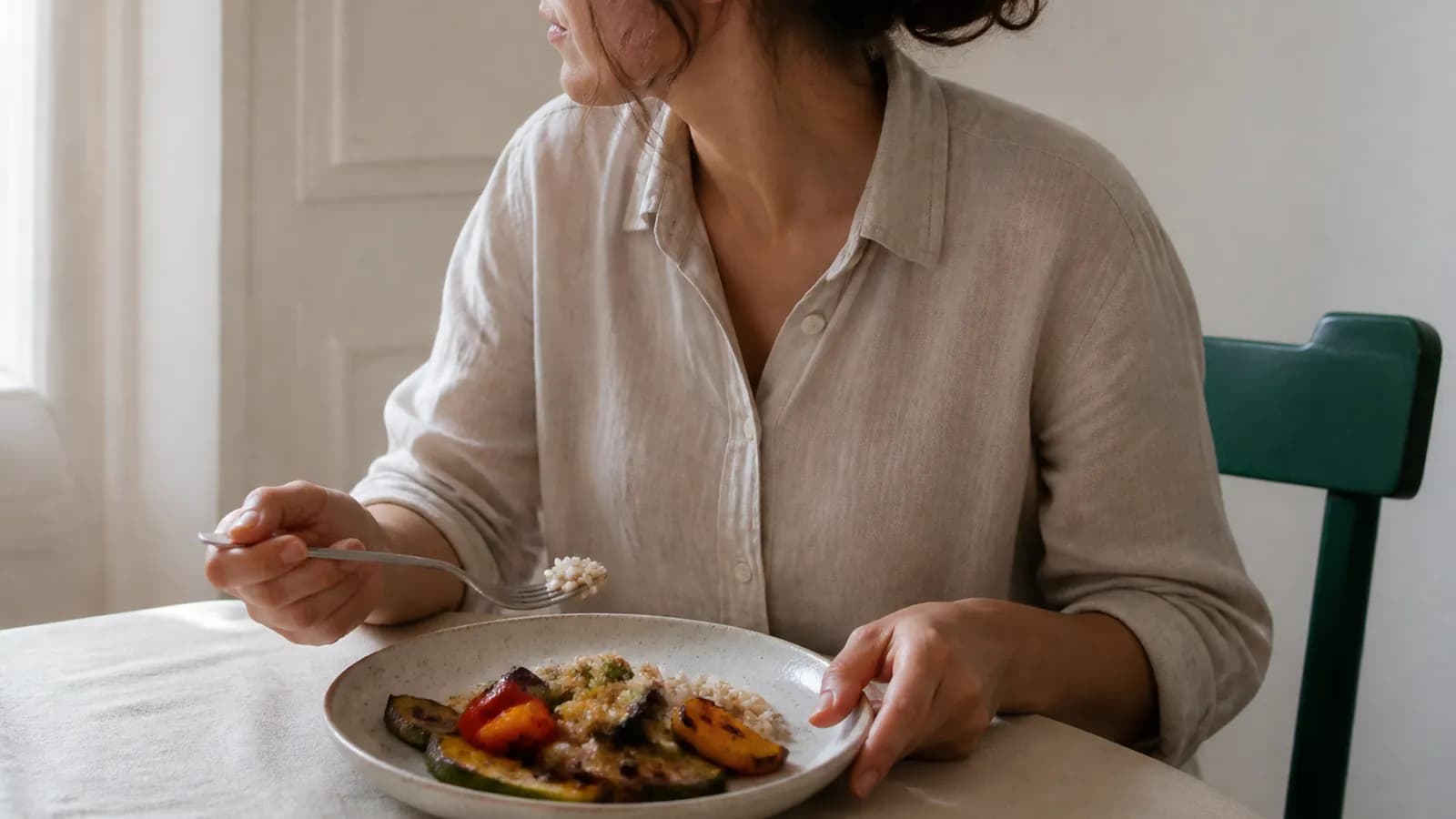 Femme adulte à une table de cuisine, devant un déjeuner simple de légumes et de riz, lumière du matin.