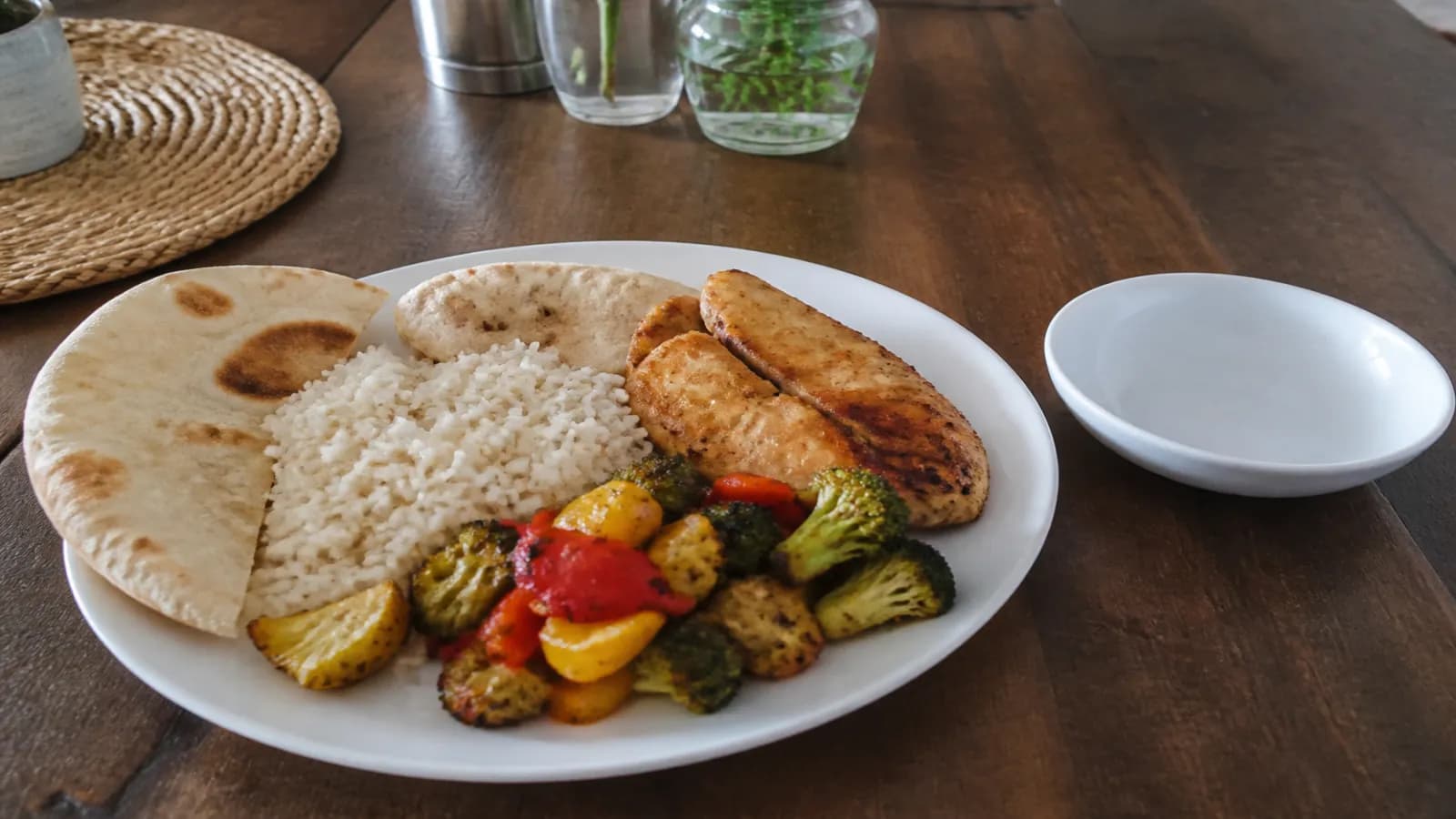 Assiette un peu plus généreuse : riz, poulet, légumes rôtis et pain, petit bol vide à côté, table en bois clair.